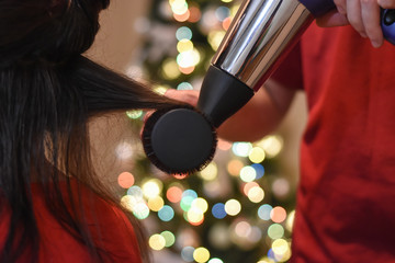 Hairdresser drying long hair with hair dryer. Making hairstyle for Christmas holidays. Concept of...