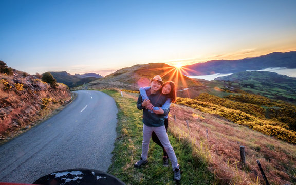 Couple enjoys beautiful Akaroa scenery near Christchurch in New Zealand. Romantic couple goes on road trip. A pair of couple goes on honeymoon in natural landscape. Happiness image of a young couple.