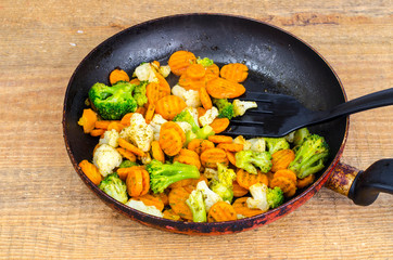 Stewed vegetables in oil on old pan, wooden table