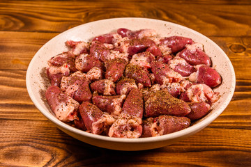 Ceramic plate with raw chicken hearts on wooden table