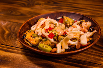 Ceramic plate with different sea food and olives on wooden table