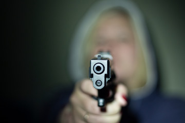 A woman holds a gun in her hand and points it at the camera . Focus on the front of the gun.