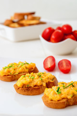 White plate with toasts and scrambled eggs, chive herbs and cherry tomatoes on white table background. Grilled bread with scrambled eggs and vegitable.