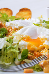 Classic French salad, great salad Lyonnaise. Dish with green leaves of lettuce, Dijon mustard sauce with pieces of fried bacon, grilled French bread, toasts and 2 poached eggs on the top.