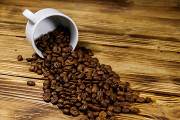 Roasted coffee beans spill out of cup on wooden table