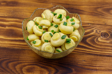 Glass bowl with pickled champignons. Marinated mushrooms on wooden table