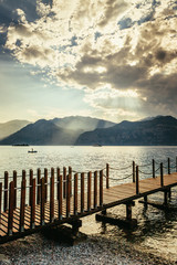 Scenery with wooden dock pier extending over blue lake water and mountains