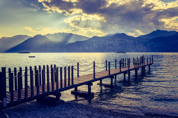 Scenery with wooden dock pier extending over blue lake water and mountains