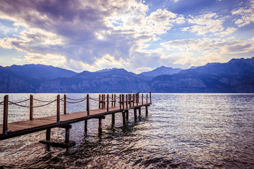 Scenery with wooden dock pier extending over blue lake water and mountains