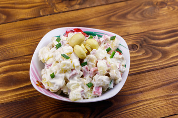 Potato salad with marinated mushrooms, sausage, onion and mayonnaise on wooden table