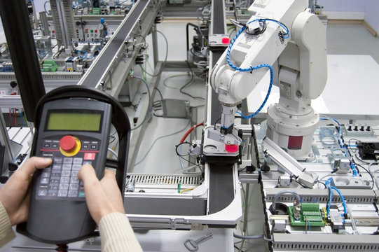 Man is holding teach panel (tablet) to control a robotic arm which is integrated on smart factory manufacturing line. industry 4.0 automation line which is equipped with sensors and robotic arm.