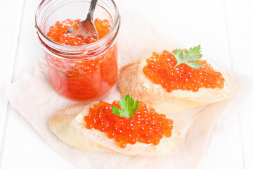 Glass jar of red caviar and snacks on white background