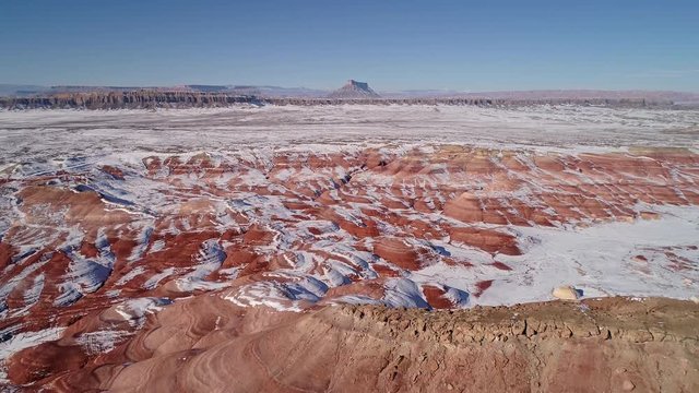 Aerial view of eroded cracks in the red desert of Utah with snow moving backwards viewing the Mars like vast landscape.