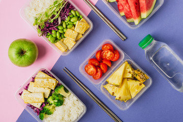 Two healthy asian-style plant-based lunch boxes knolled together on blue and pink background, flatlay