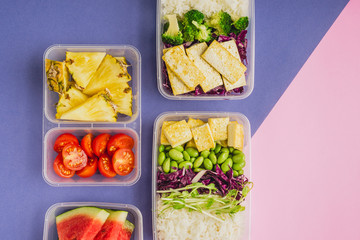 Two healthy asian-style plant-based lunch boxes knolled together on blue and pink background,...