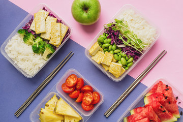 Two healthy asian-style plant-based lunch boxes knolled together on blue and pink background, flatlay