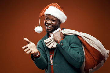 Modern Santa Claus. Smiling emotional man posing in green coat and red sweater, with santa hat and...