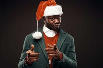 Modern Santa Claus. Smiling man in green coat and red sweater, with santa bag in hand. Studio shot, black background