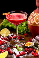 Glass of red cherry cocktail at decorated with berries, lemon and mint wooden table background.