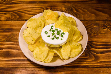 Ceramic plate with potato chips and glass bowl with sour cream on wooden table