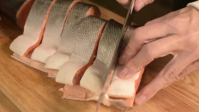 Close-up of female hands are cutting with a knife a large salmon on a wooden table of home cooking