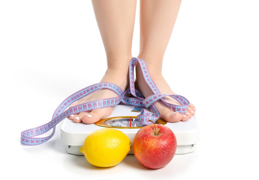 Female feet weighing scale centimeter apple lemon on a white background isolation