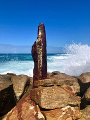Sea splashing against rocks and rusty metal looking like a madonna figure