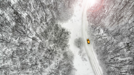 Aerial. Beautiful rural country road between forest with yellow car in winter season.