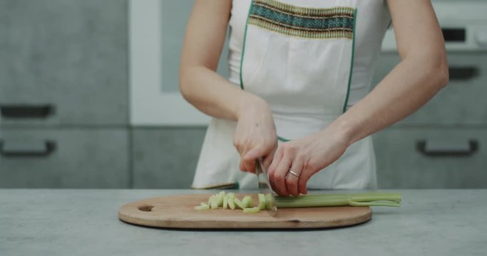 Woman in her kitchen closet cut a big celery with a big knife on the chopper , professional cuts.