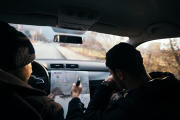 Criminals sitting at sunset in a car, looking at the city map and planning their next move.