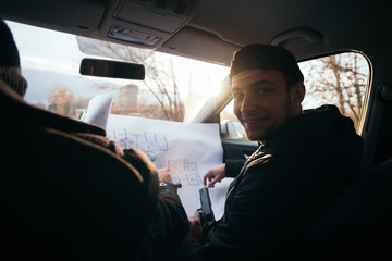 Two violent robbers sitting in a car looking at a blueprint of the building they want to rob while...