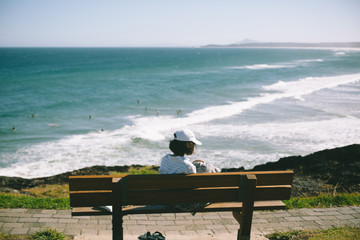 young girl sitting on a bench in front of sea