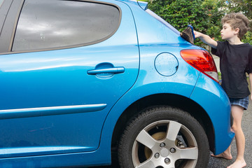 Fototapeta na wymiar Boy earning pocket money cleaning blue compact car