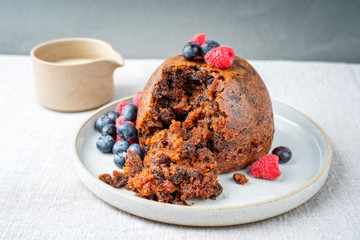 Traditional Australian plum pudding as closeup with fruits and vanilla rum sauce on a dessert plate with copy space