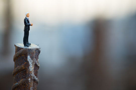 Miniature people: businessman thinking and standing at construction site