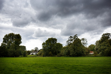 water meadows lined with trees with cloudy sky and cottages
