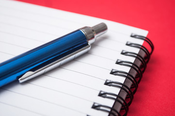 closeup of blue pen on spirales note book on red background