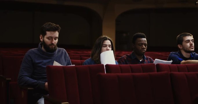 Medium shot of actors memorizing their lines while sitting in the auditorium