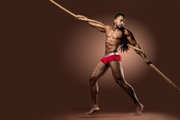 Muscular African American Black athletic fitness model wearing red underwear  holding a thick rope...