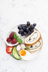 A healthy farmer family breakfast snack. Slices of cereal bread with nuts, poppy rolls, halves of boiled egg, cucumber, radish, fresh juicy vegetables and berries. Top View.