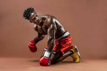 Muscular African American Black male sweaty boxer on knees,  knocked down trying to get up with dramatic lighting with a brown background  