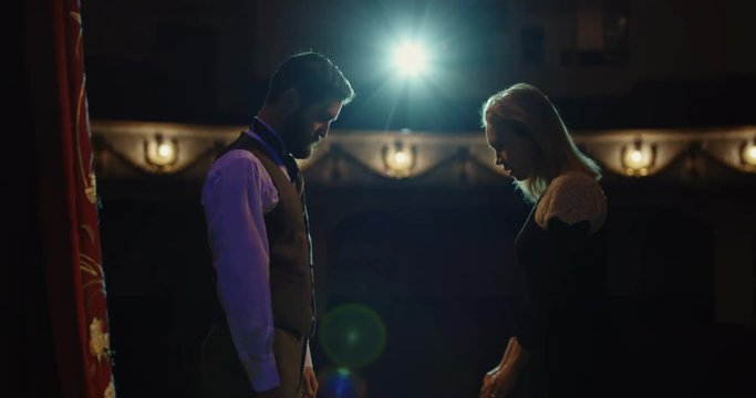 Medium shot of an actor and an actress performing a romantic scene in the theater after the curtains are opened