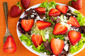 Vegetarian delicious fresh salad with purple and green lettuce leaves, strawberries and goat cheese on orange tablecloth.