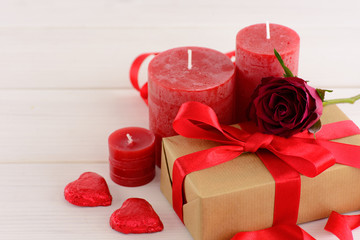 Valentines day red background with red roses on a white wooden table. A gift box decorated with hearts and candles on the table.