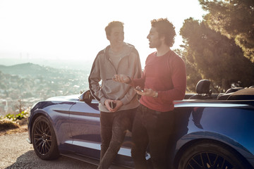 Two guys at sunrise laughing with blue car in viewpoint