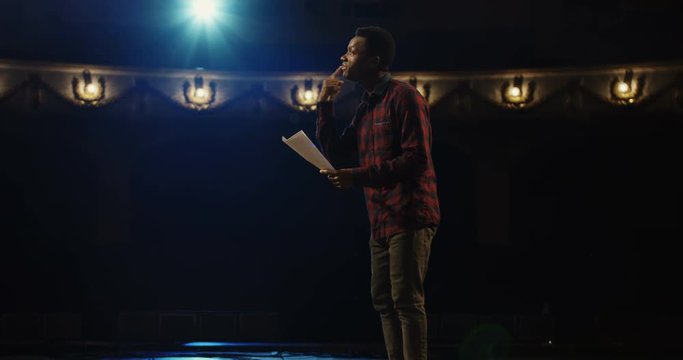 Medium close-up shot of an actor performing a monologue in a theater while holding his script