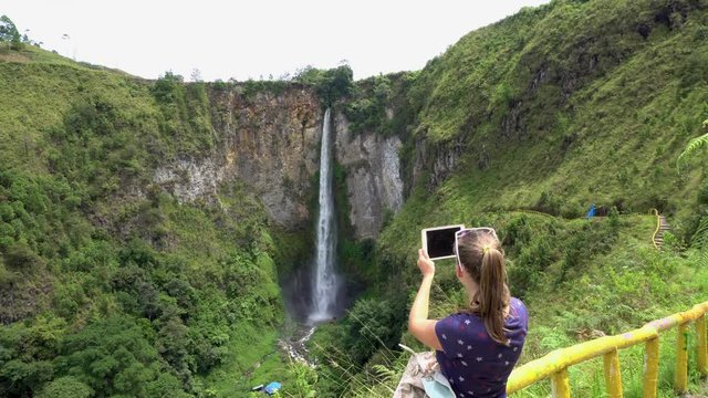 Cinemagraph of Young Woman Taking Photo of Sipiso Piso Waterfall, North Sumatra, Indonesia. Female Traveler living Active Lifestyle