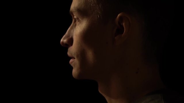 Young man falls light on the face in dark. The profile of a man in the dark on which the light falls. Warm light on the guy's face