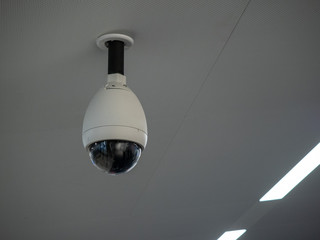 White circular surveillance camera on ceiling in a public setting attached to white ceiling