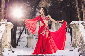 Deurstickers beautiful young girl dancing belly dance in red dress in winter in a park on the snow. © Marina Varnava